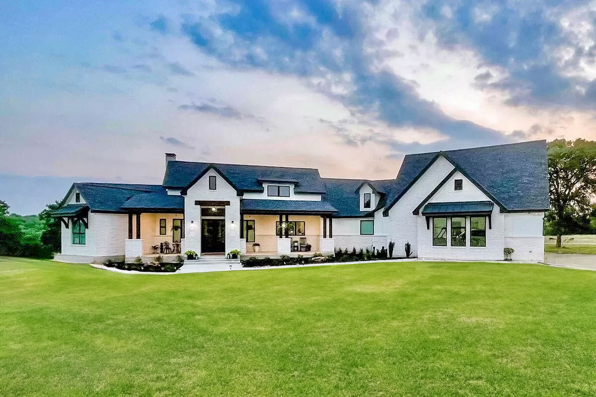 Exterior rendering of Hill Country House Plan 915047CHP from Architectural Designs, a single-level home with deep porches and an angled two-car garage