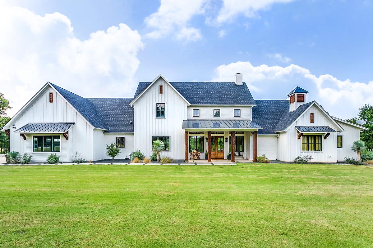 Exterior rendering of Plan 915050CHP: a two-story Modern Farmhouse with board and batten siding, multiple gabled rooflines, a wide covered front porch with centered French doors, and a 3-car attached garage